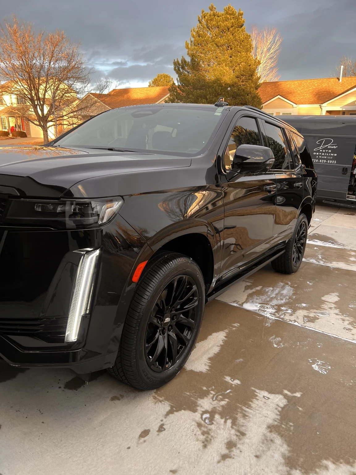 Black luxury SUV freshly detailed with the Denver Auto Detailing & Wash van in the background